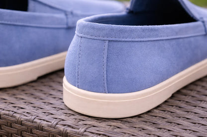 Gros plan sur mocassins bleu pastel en daim, semelle blanche, posés sur rotin.