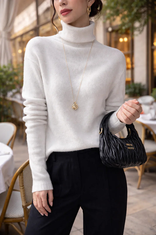 Femme portant un pull blanc col roulé, pantalon noir, sac à main noir, collier doré