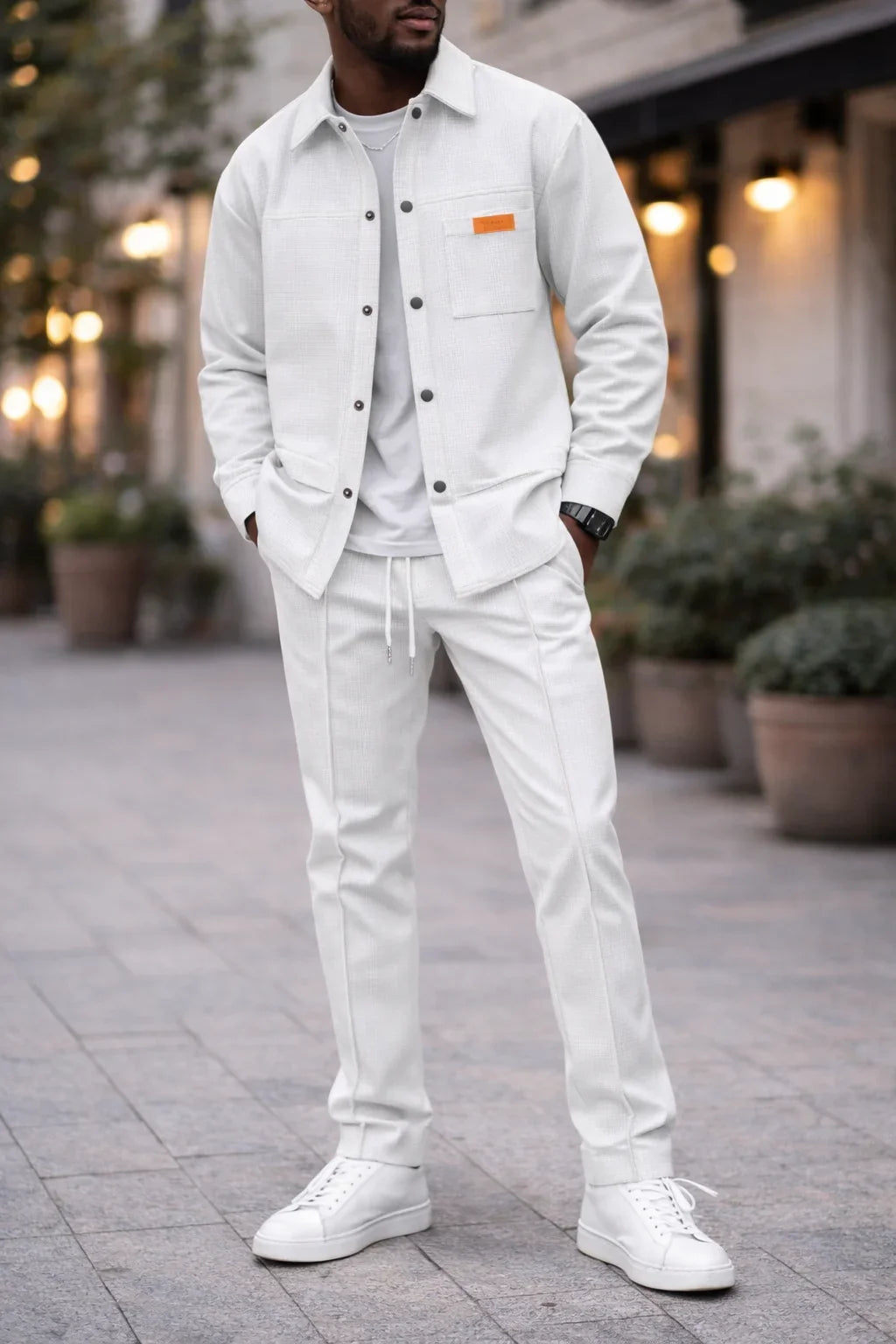 Homme portant un ensemble décontracté blanc, veste et pantalon, baskets blanches, rue urbaine.